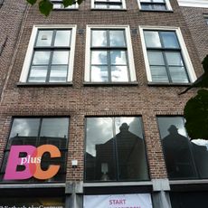 Pand met bakstenen rechte kroonlijst met barokconsoles. Onderpui verbouwd