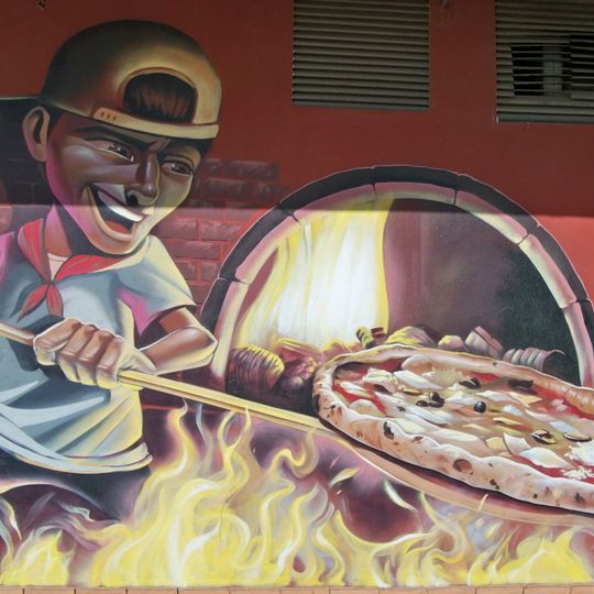 Mural representando un cocinero preparando una pizza en un horno.