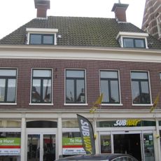 Zes traveeën breed pand onder dwars schilddak met twee hoekschoorstenen met borden