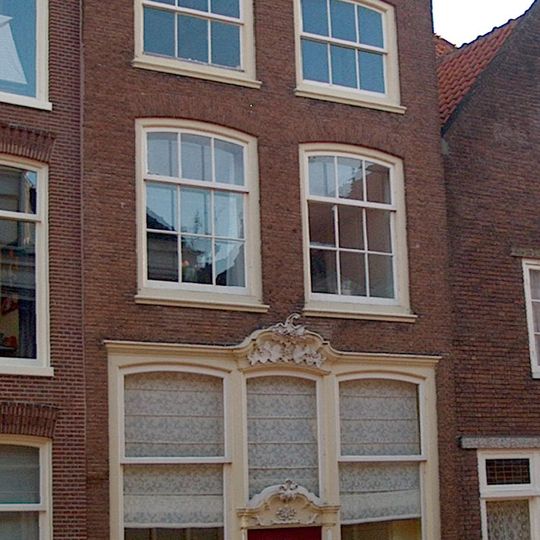 Huis met hoge bakstenen gevel met rechte kroonlijst waarop gesneden consoles en dakkapel, voor dwarskap. Venster met sterk gebogen strek en oude roeden.