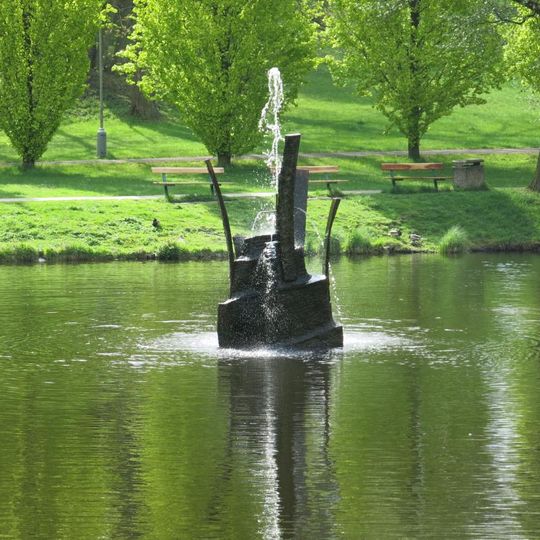 Fontána z kamene a kovu v jezírku v Husových sadech v Sokolově
